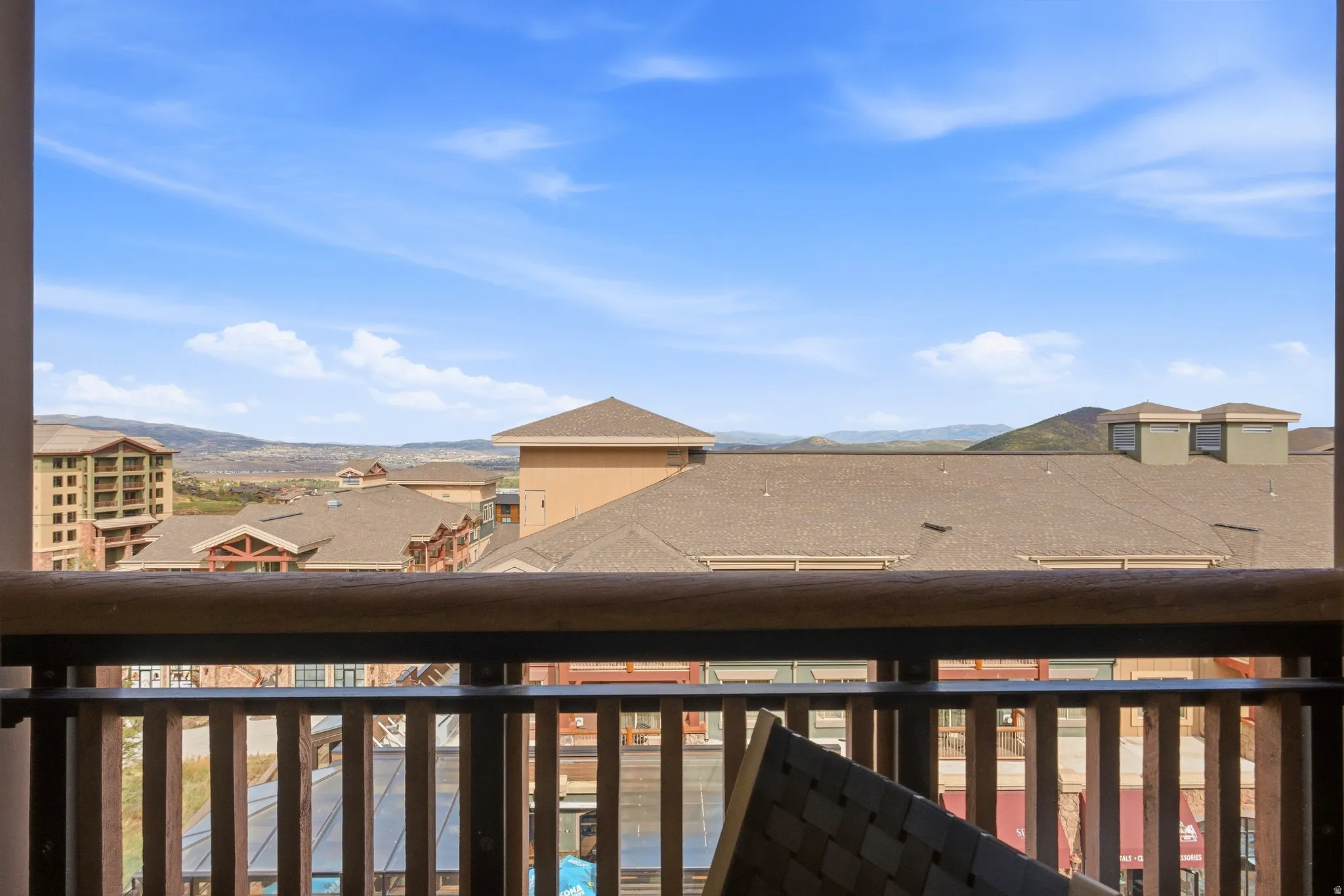 Balcony with wood and metal railing overlooking buildings with varied rooflines and distant mountainous terrain