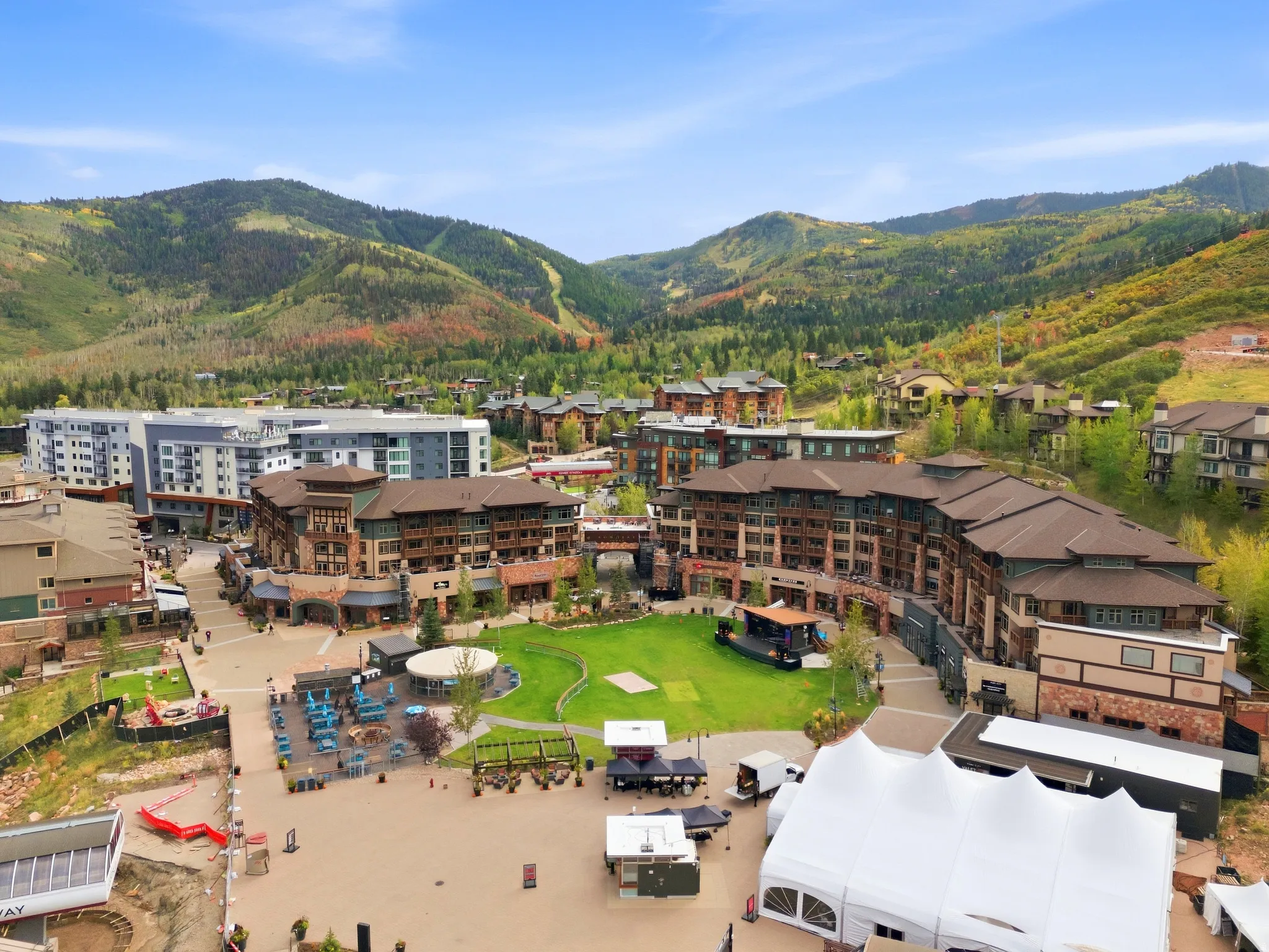 Expansive mountain backdrop, modern mixed-use development, central green space, and multiple outdoor dining areas