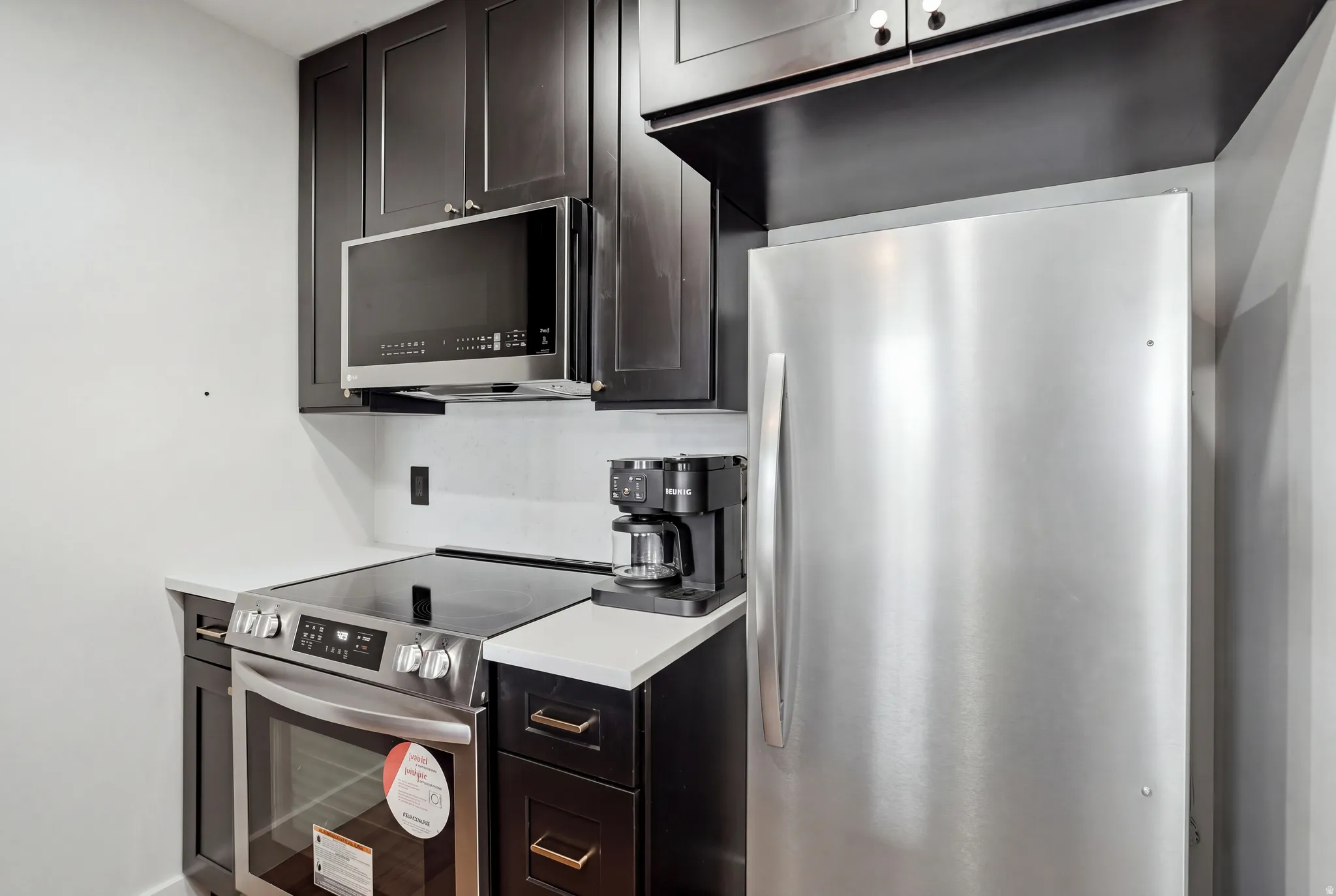 Dark wood-finish cabinetry, white countertops, built-in stainless steel microwave, stainless steel range, and stainless steel refrigerator