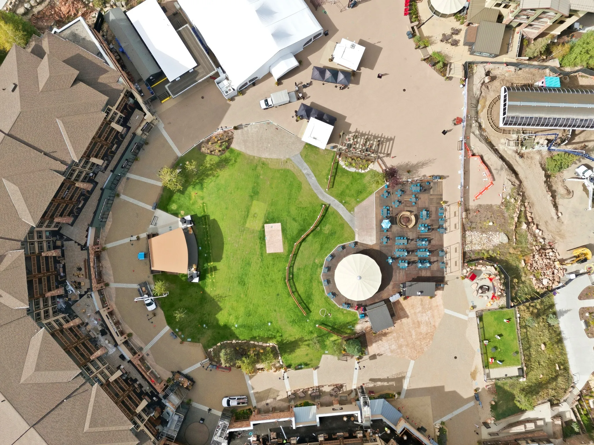 Central green space with meandering pathways, surrounded by paved plaza areas, and multiple commercial structures featuring distinct rooflines