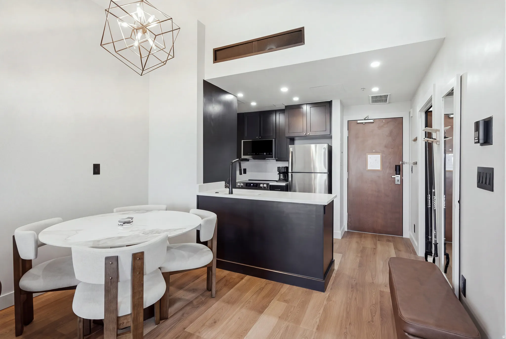 Modern open-concept living area with wood-finish flooring, a contemporary geometric chandelier, and recessed lighting