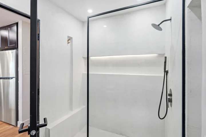 Enclosed shower with a frameless glass panel, integrated niche shelving, matte black fixtures, and a recessed ceiling light