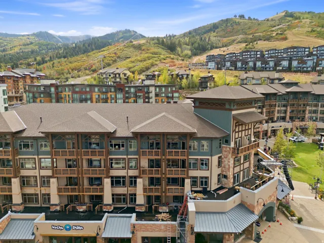 Multi-story building featuring integrated commercial spaces, multiple balconies, and visible mountain scenery