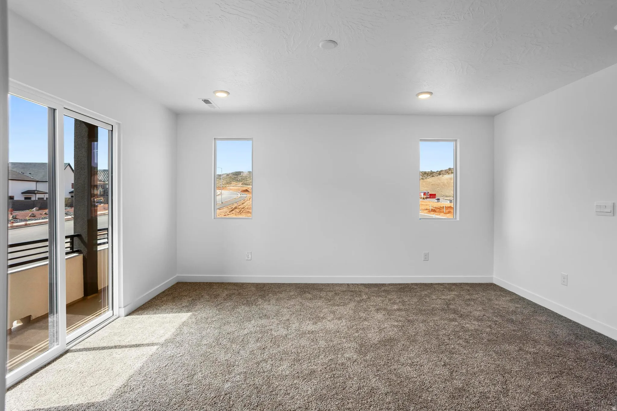 Spacious room featuring neutral carpeting, recessed ceiling lighting, and a sliding glass door to a balcony with black railings