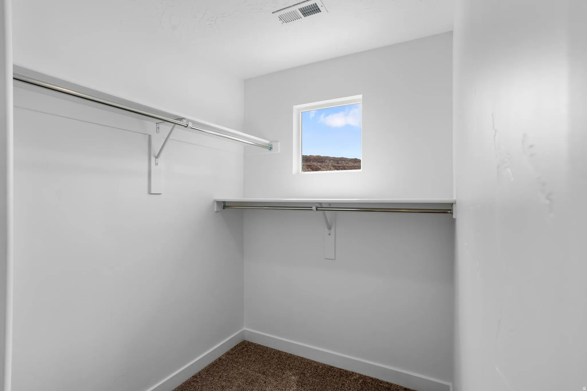 White interior walls, shelf and rod storage system, small window, carpeted flooring, and ceiling vent