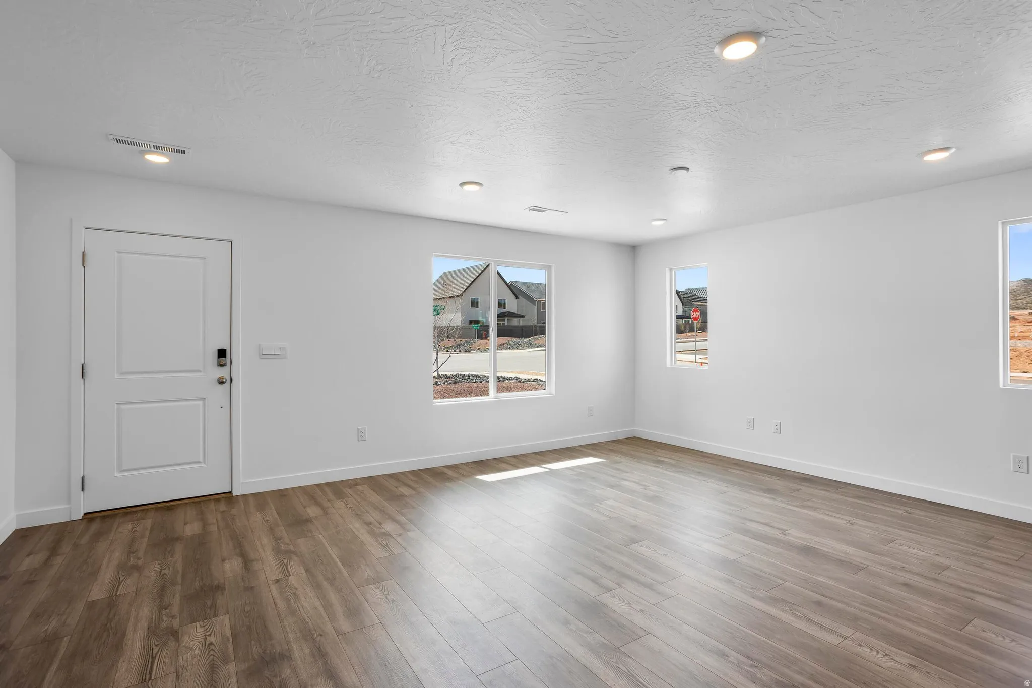 Spacious room featuring wood-finish flooring, multiple windows, recessed lighting, and a white paneled door