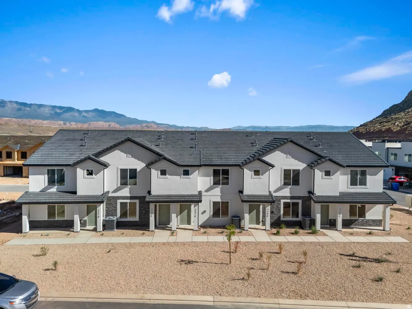 Modern townhome architecture featuring a multi-tone exterior, dark shingle roof, covered entries, and a gravel landscape