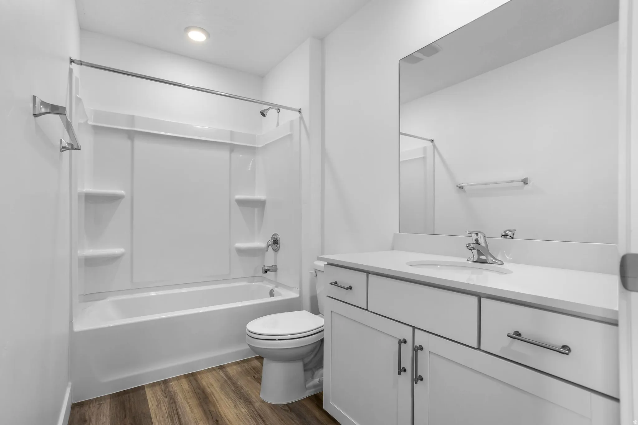 Tub/shower combination with a durable surround, single-basin vanity with white cabinetry, wood-finish flooring, and an integrated mirror