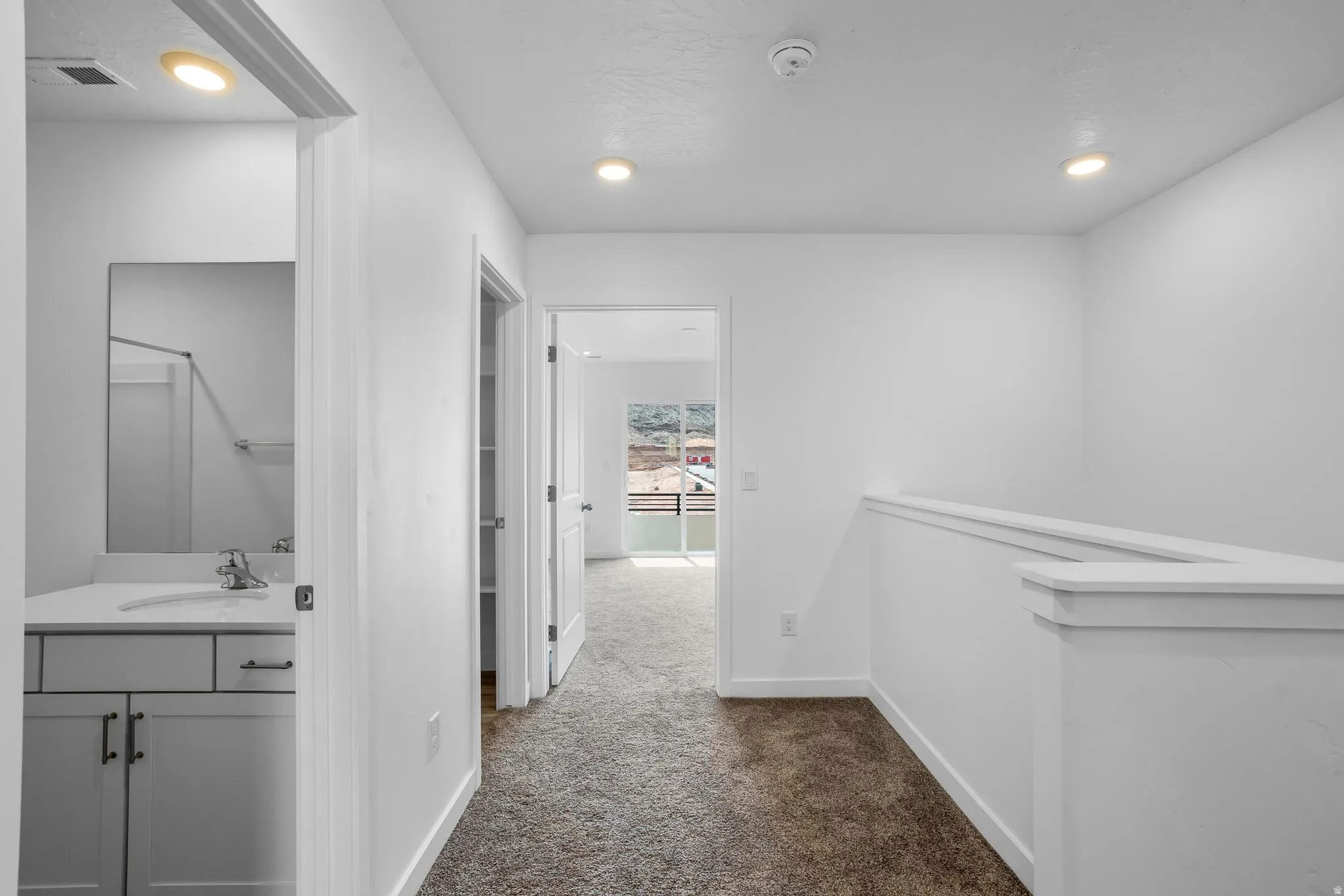 White interior finishes, recessed lighting, carpet flooring, railing, vanity with undermount sink