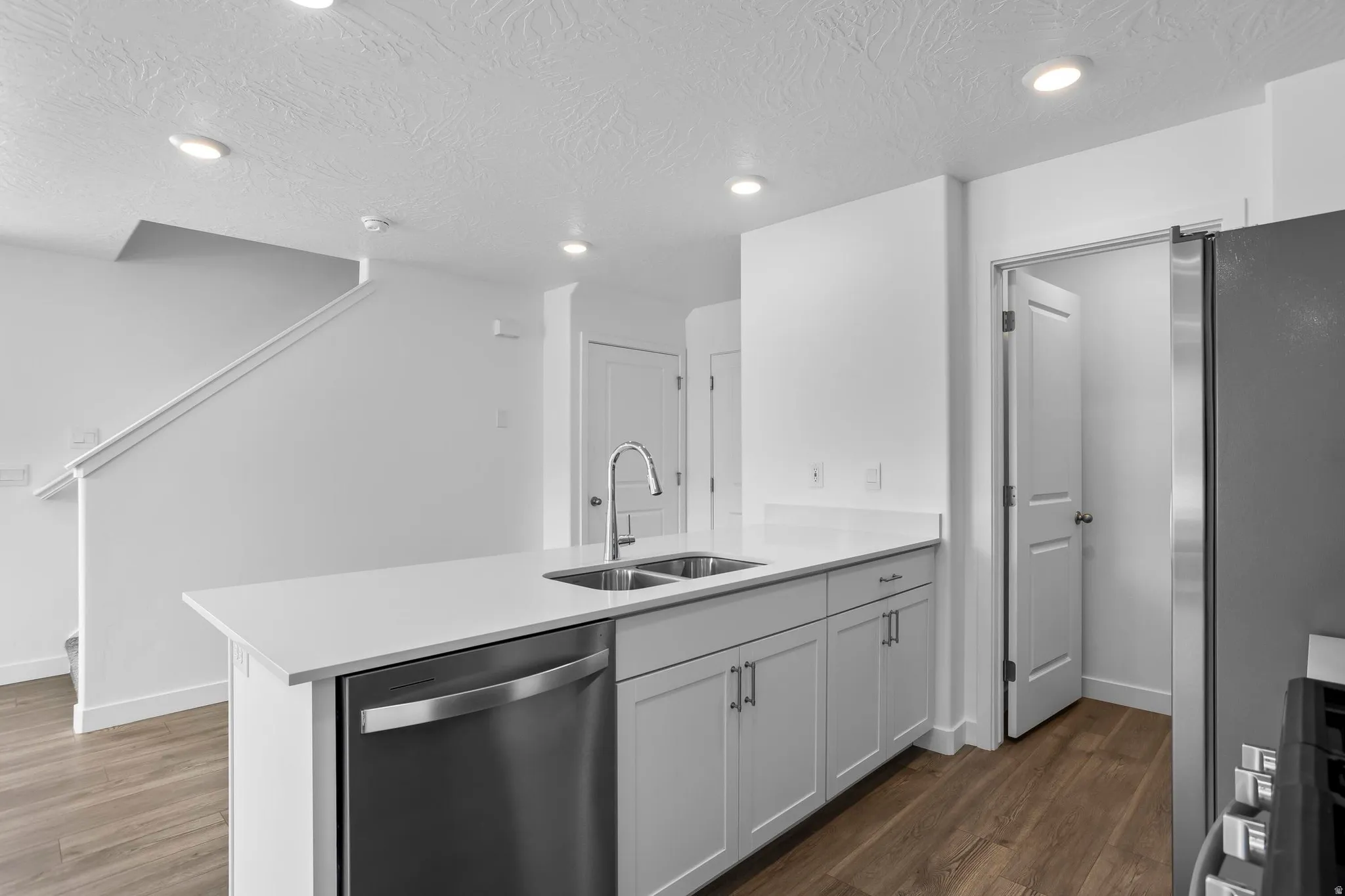 Kitchen island with integrated stainless steel sink and dishwasher, white cabinetry, and light-toned countertop