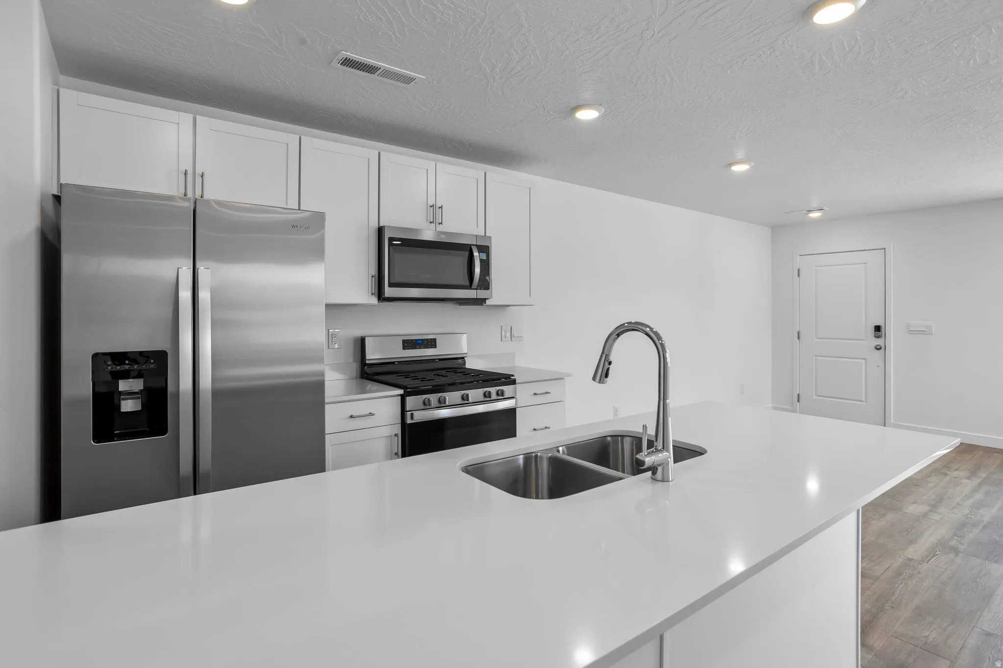 White shaker-style cabinetry, stainless steel appliances, a double basin stainless steel sink, and recessed lighting