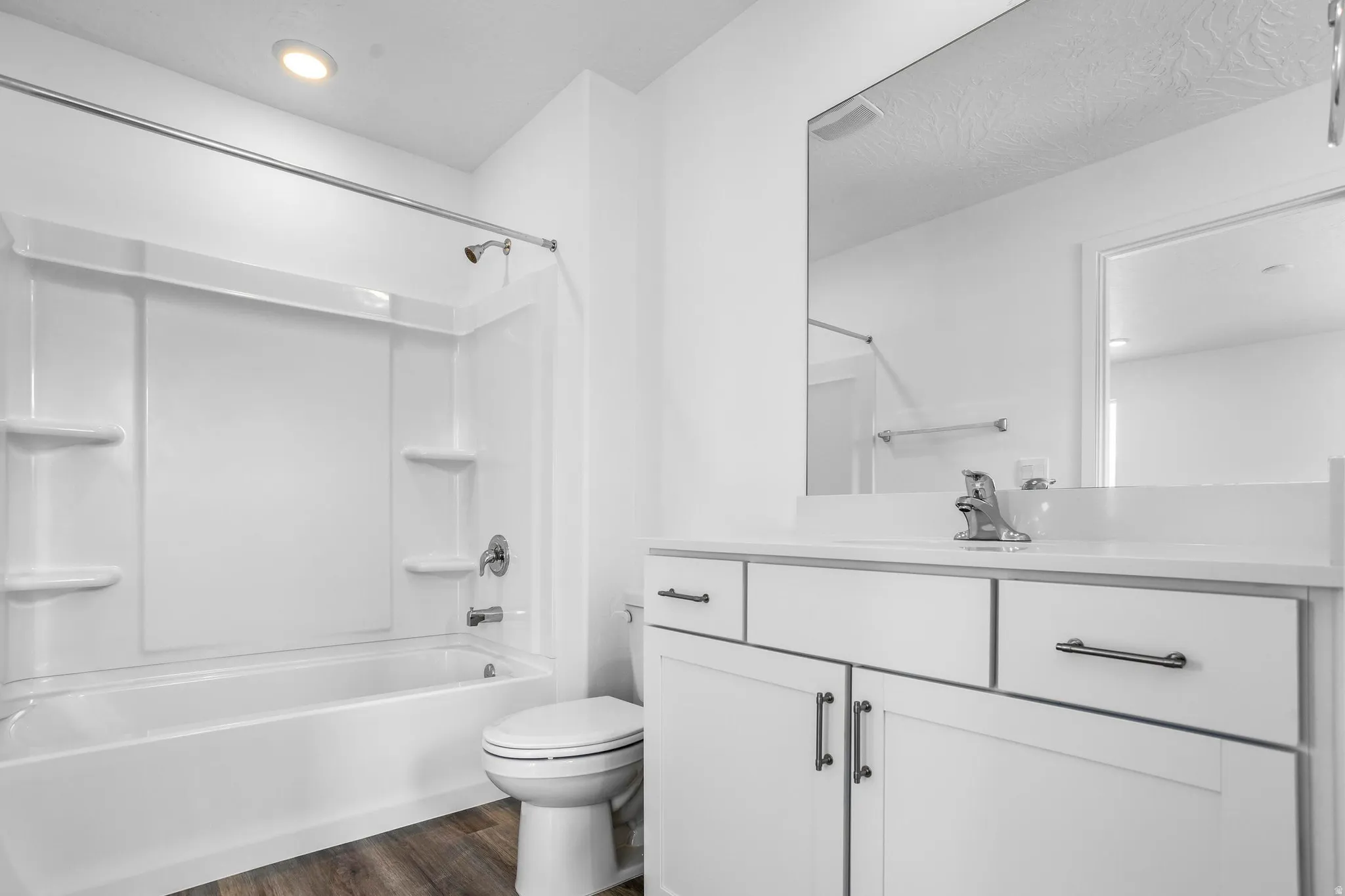 Bathroom featuring a white vanity with cabinet storage, a single basin sink, a large mirror, a white toilet, and a white tub with shower