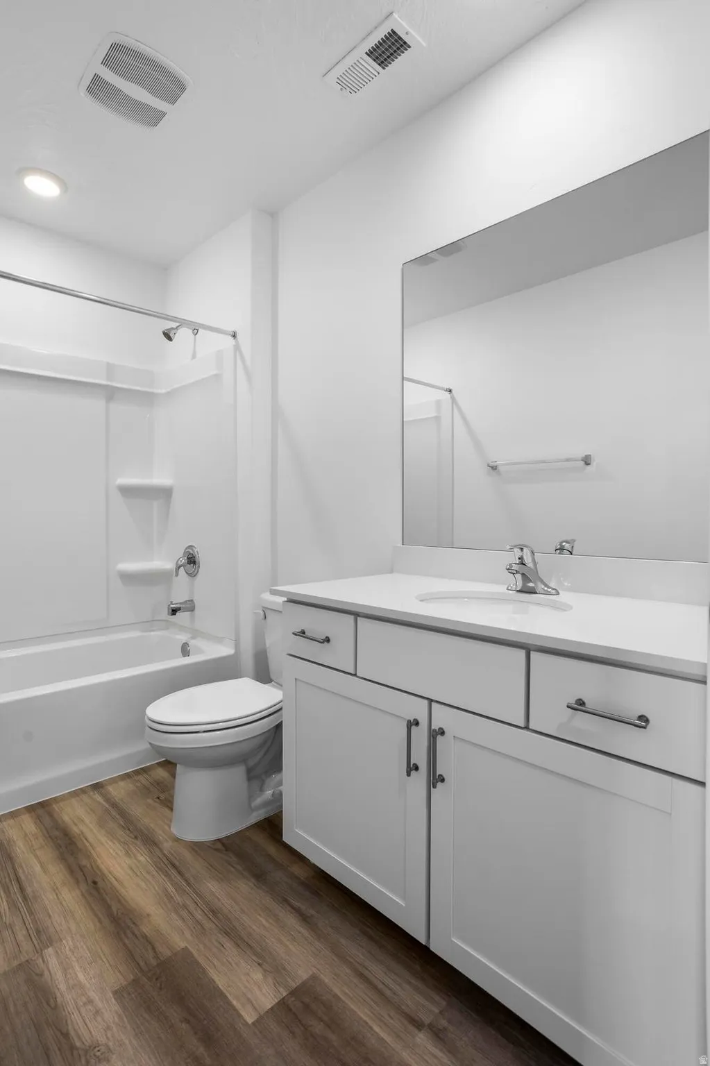 Bathroom featuring a white vanity with white countertop, wood-finish flooring, a full-width mirror, and a white tub with shower