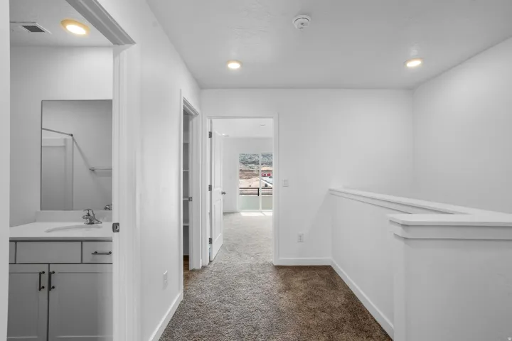 White interior finishes, recessed lighting, carpet flooring, railing, vanity with undermount sink