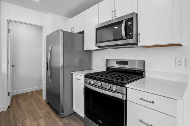 Kitchen featuring white shaker cabinetry, stainless steel appliances, white countertops, and wood-finish flooring