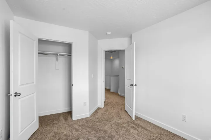 White interior walls, neutral carpet flooring, and a built-in closet with a hanging rod