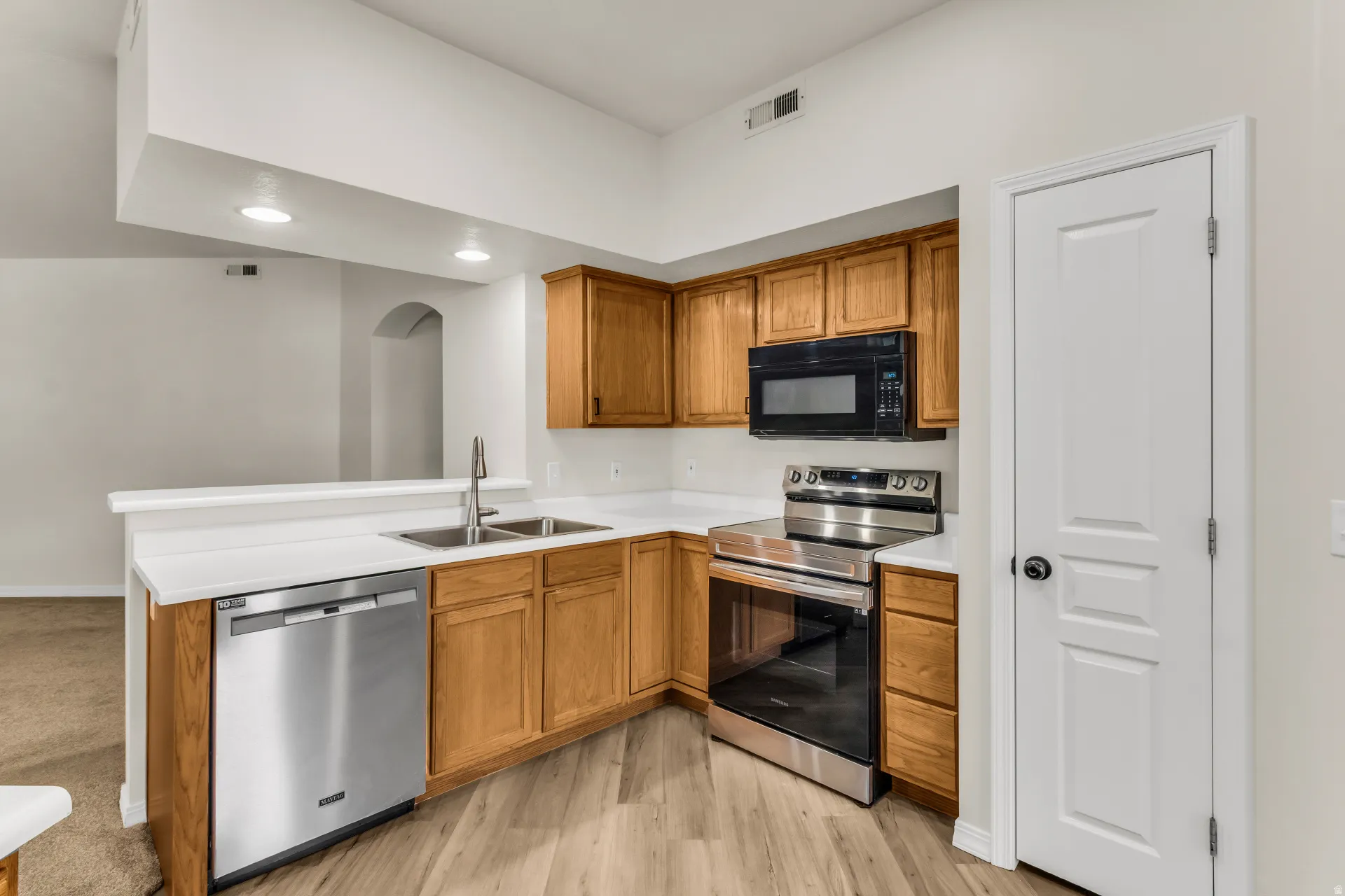 Wood-finish flooring with recessed lighting, stainless steel appliances, wood cabinetry, and a double basin sink. All appliances included.