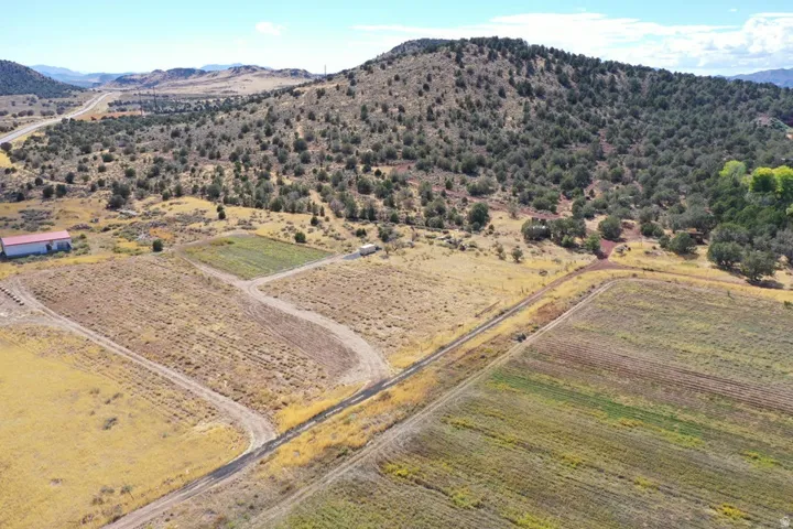 Expansive land featuring a distinct agricultural field, a separate cultivated plot, a large outbuilding with a red roof, and a prominent hillside with dense tree coverage