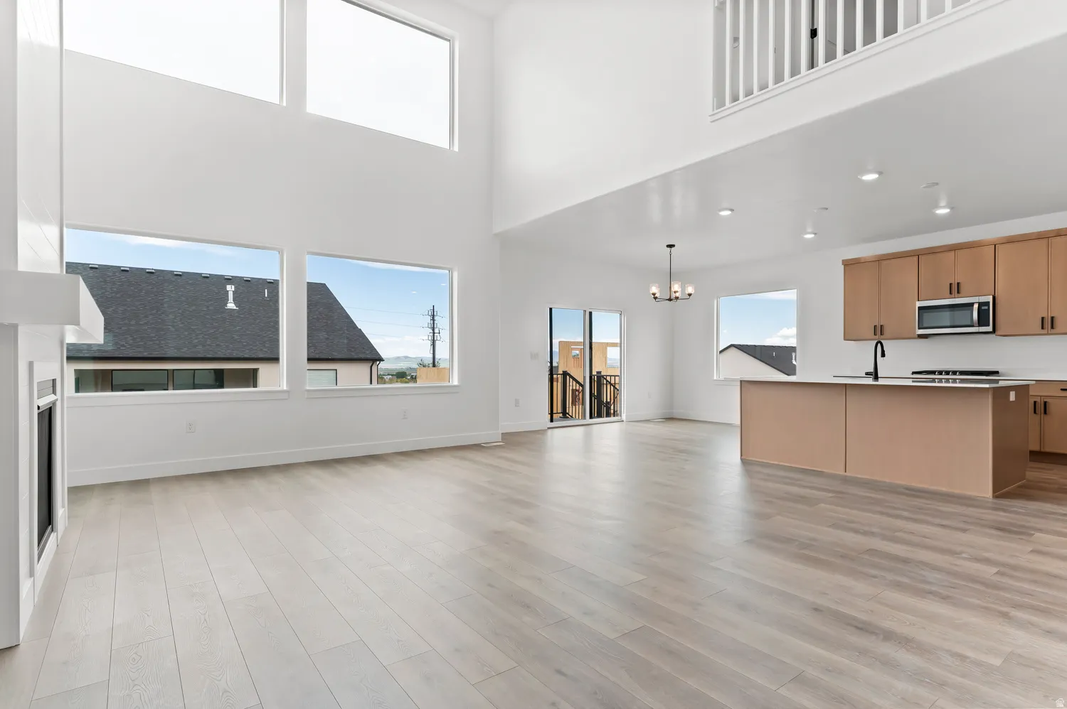 Two-story ceiling, large windows, wood-finish flooring, fireplace, and a kitchen island with built-in sink and stove