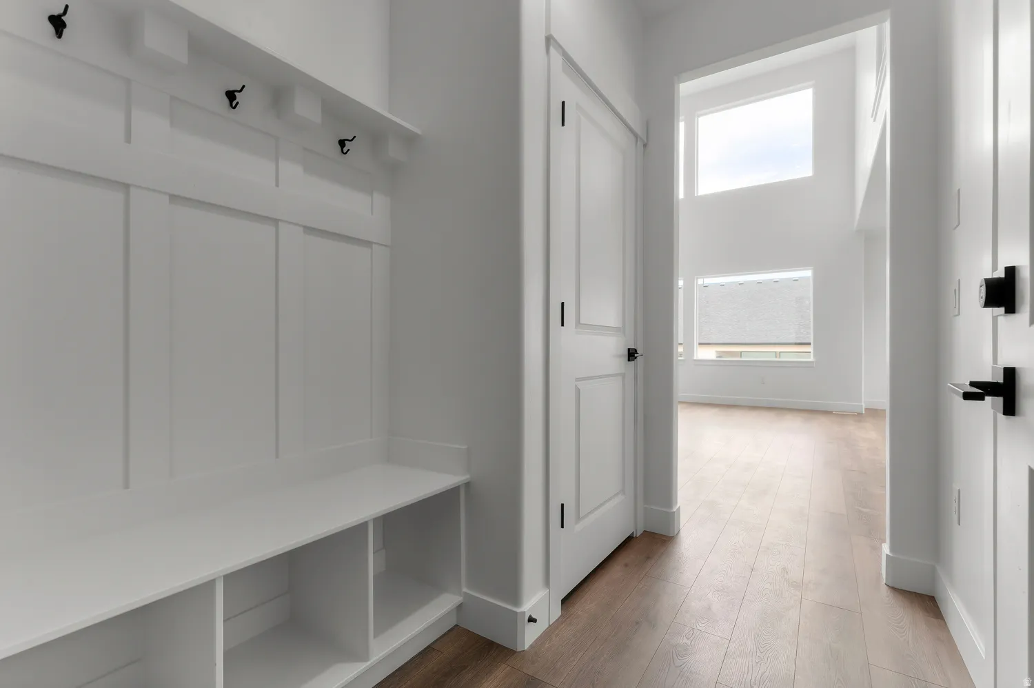 Entryway featuring a built-in bench with storage, wood-finish flooring, and white paneled doors with matte black hardware