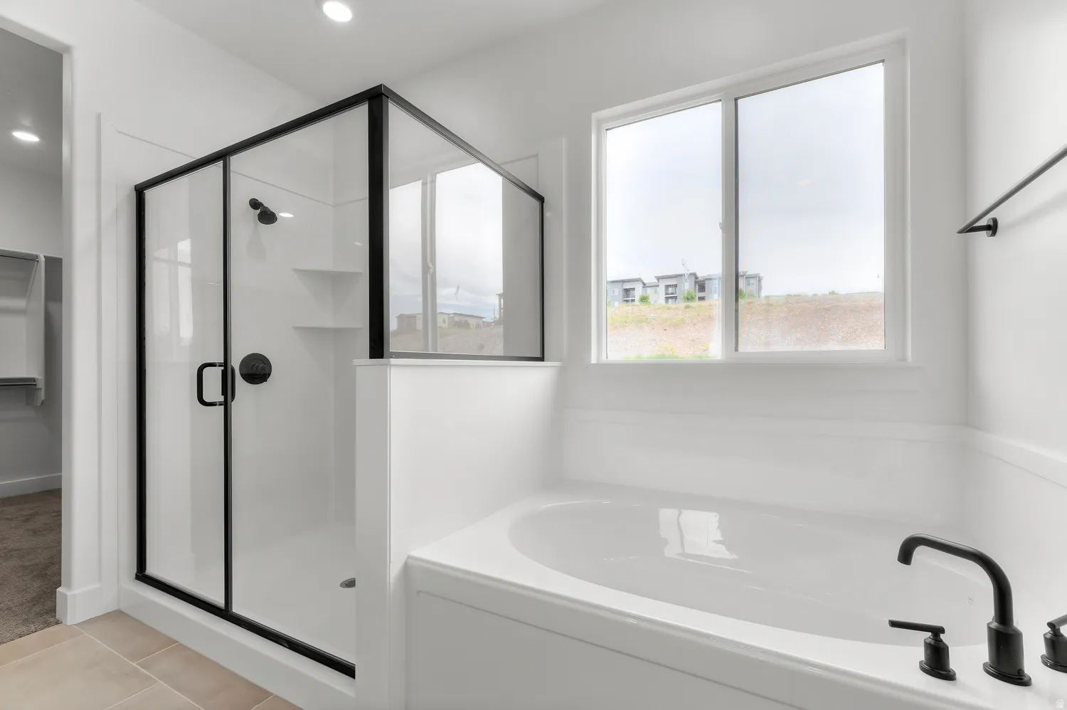 Spacious soaking tub with matte black fixtures, separate shower with black-framed glass enclosure, built-in shower shelving, recessed lighting, and tile flooring