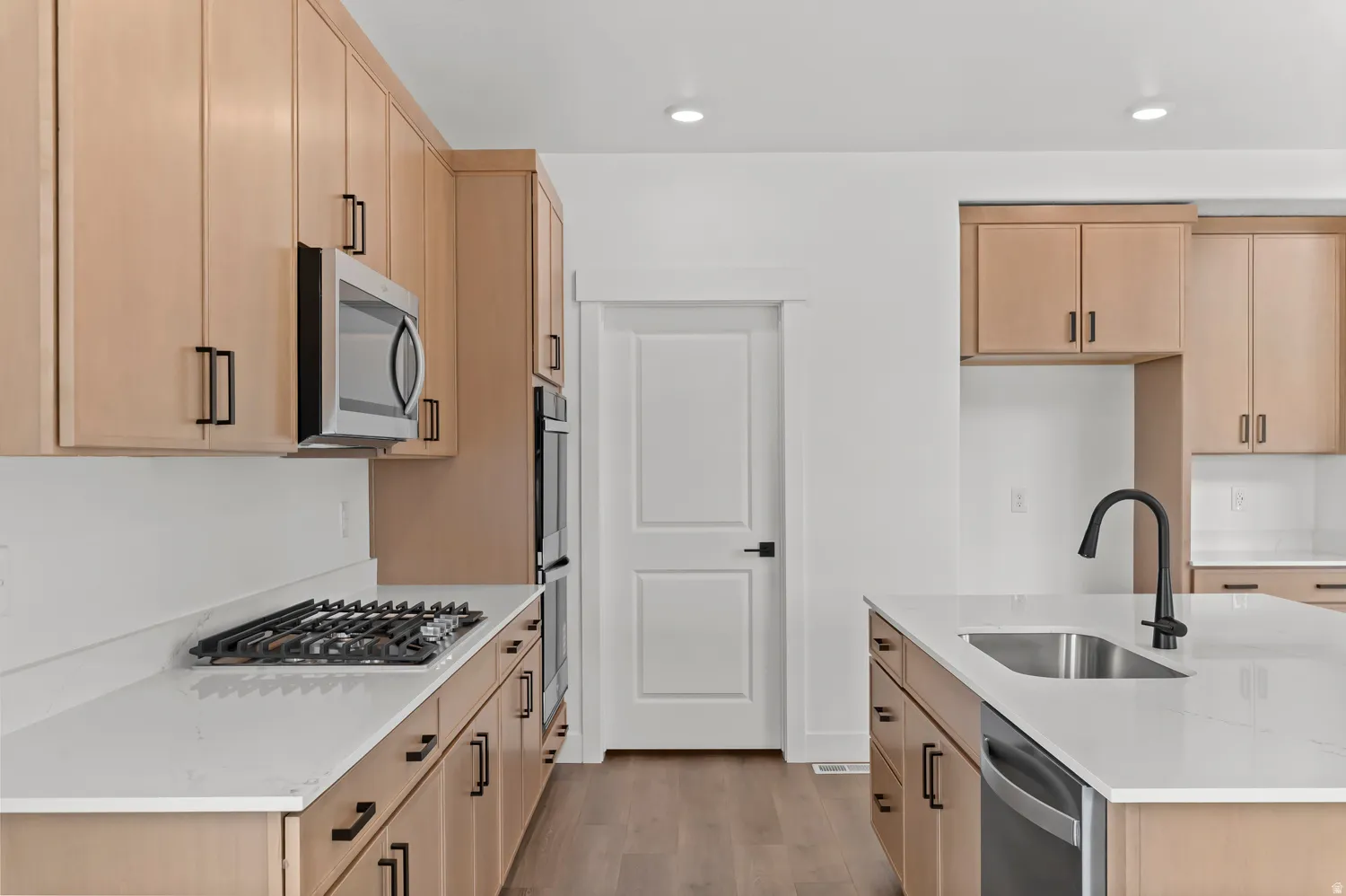 Kitchen featuring wood-finish cabinetry, stainless steel appliances, white countertops, and a center island with an integrated sink