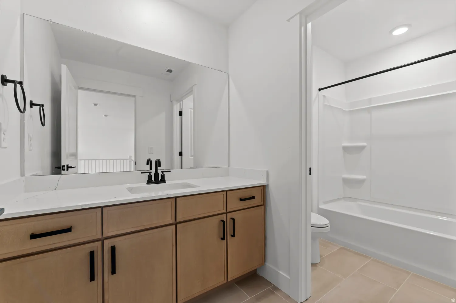 Extended vanity with light wood-finish cabinetry, white countertop, integrated sink, and black fixtures