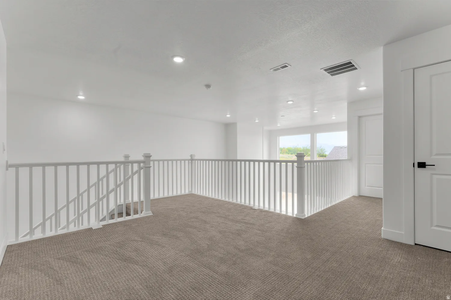 Carpeted loft area featuring white painted railings, recessed lighting, and white paneled doors with black hardware