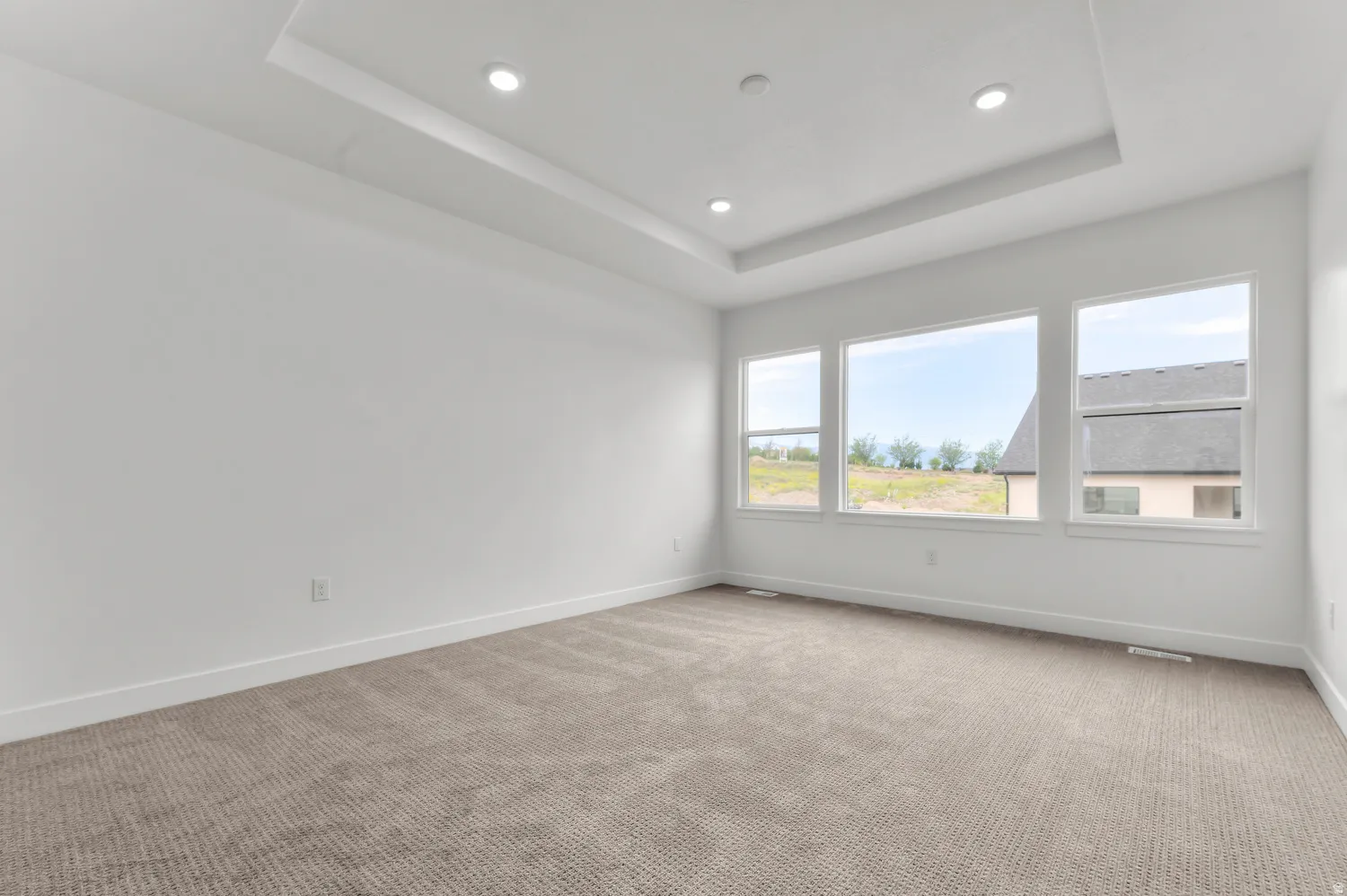Tray ceiling with recessed lighting, multiple large windows, and neutral carpeting