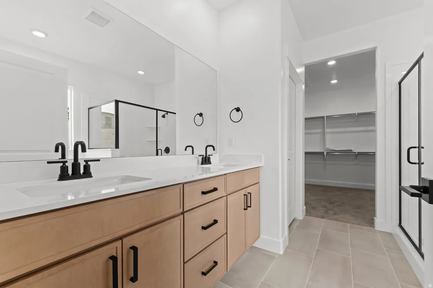 Dual vanity with light wood-finish cabinetry, matte black fixtures, and a large wall-mounted mirror