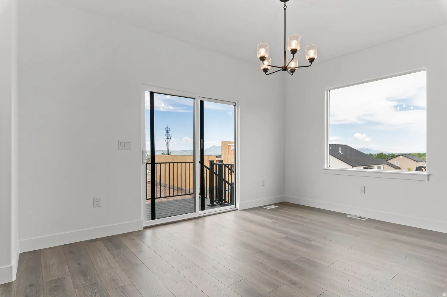 Wood-finish flooring, white walls, modern chandelier, sliding glass door, and large window