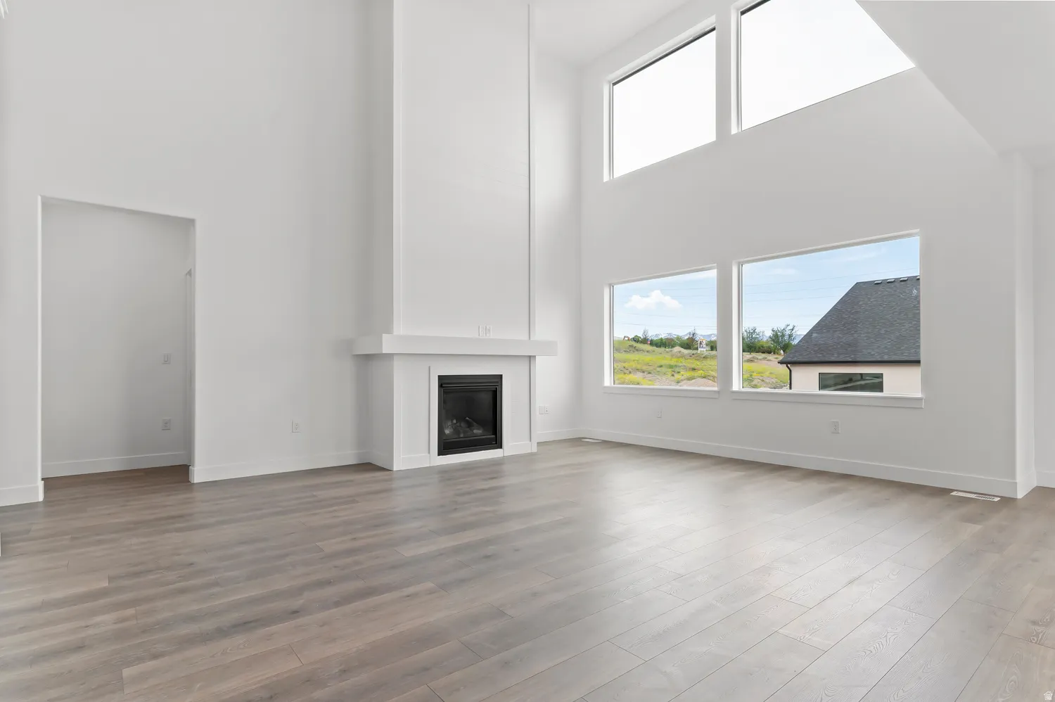 Spacious room featuring high ceilings, wood-finish flooring, a contemporary fireplace with a white mantel, and multiple large windows