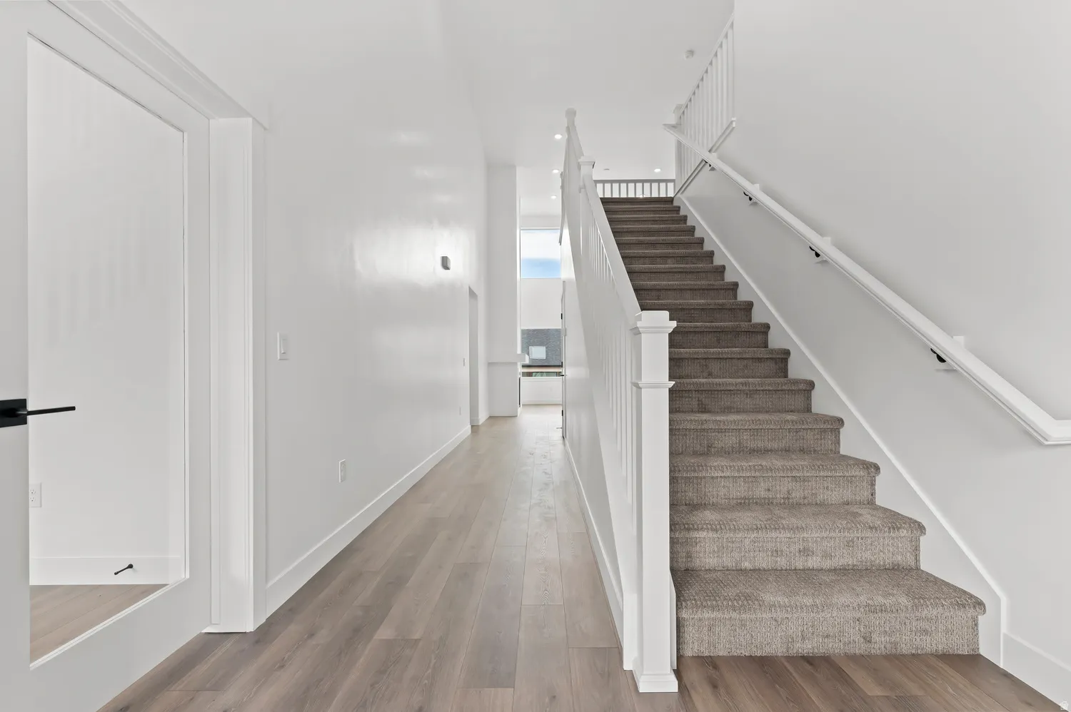Hardwood-finish flooring, white walls, carpeted staircase, and white banister