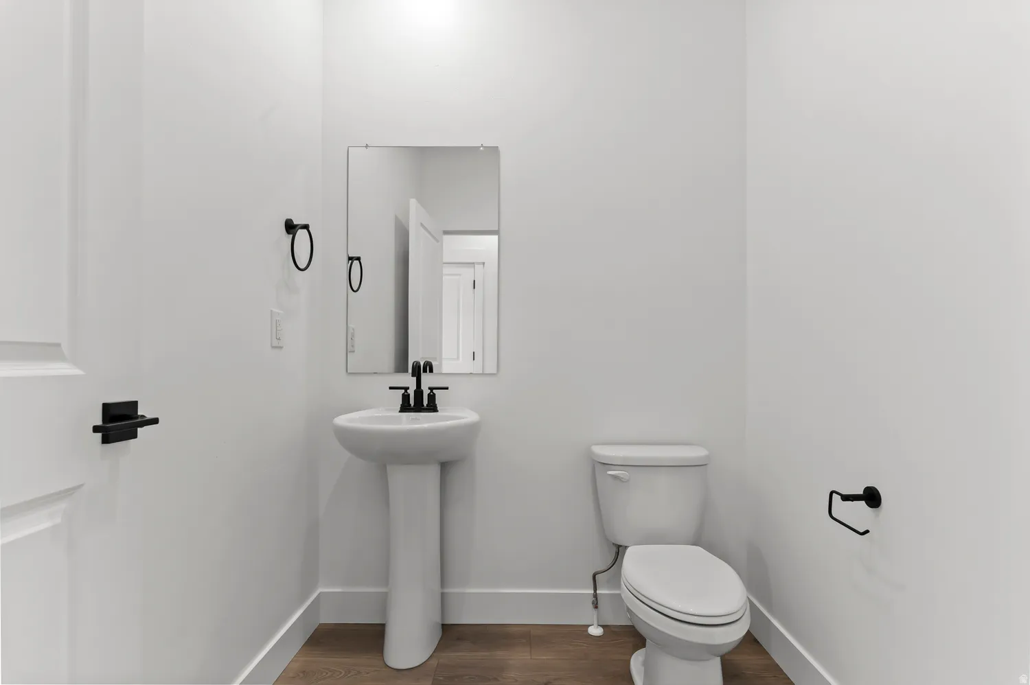Pedestal sink with a matte black faucet, rectangular mirror, and wood-finish flooring