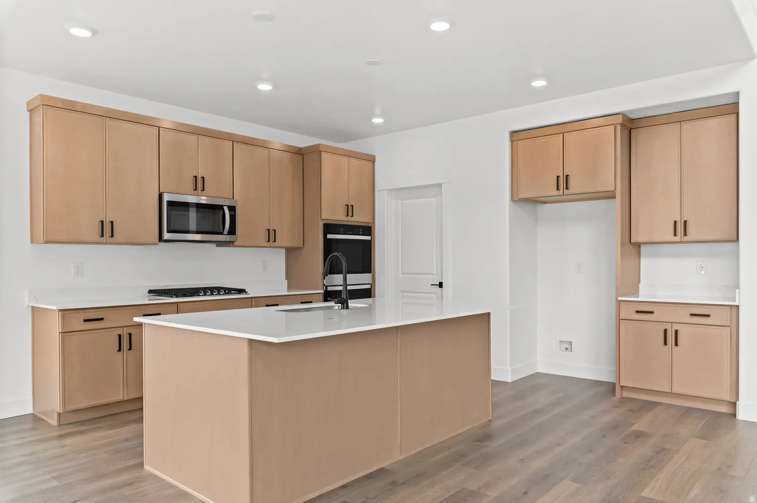 Kitchen featuring light wood-finish cabinetry, white countertops, a central island, stainless steel microwave, and wood-finish flooring
