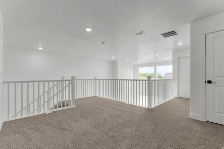 Carpeted loft area featuring white painted railings, recessed lighting, and white paneled doors with black hardware