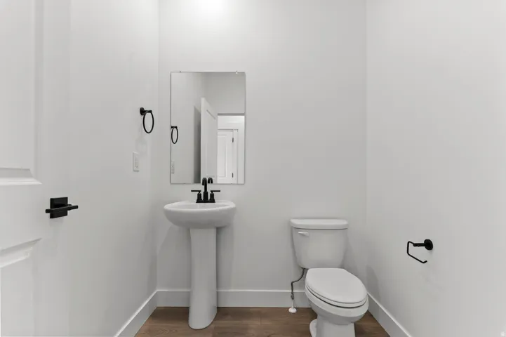Pedestal sink with a matte black faucet, rectangular mirror, and wood-finish flooring