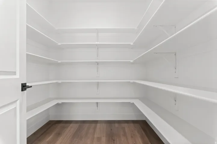 Spacious pantry featuring extensive white shelving, wood-finish flooring, and a modern black door handle