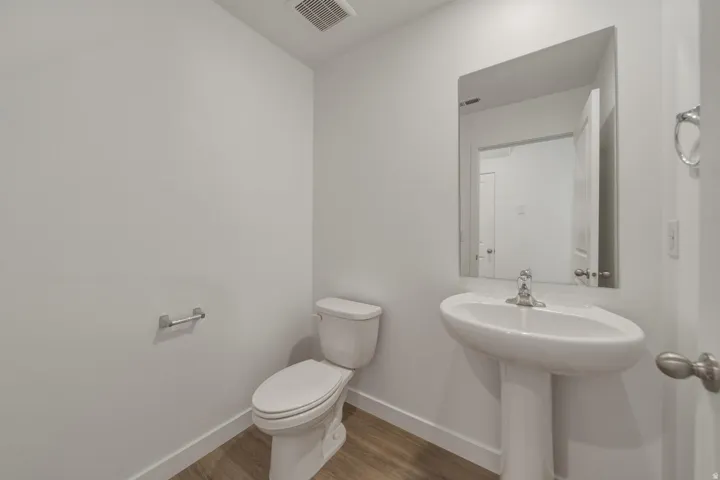 Pedestal sink with a polished chrome faucet, rectangular wall-mounted mirror, and wood-finish flooring