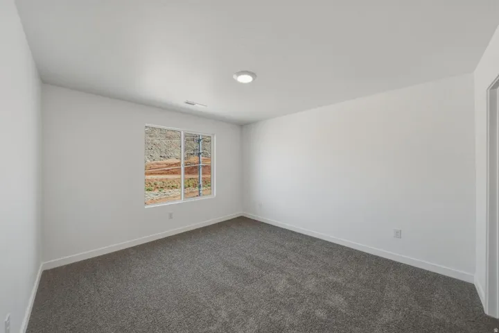 Recessed ceiling lighting, white walls, gray carpet, and a window providing natural illumination