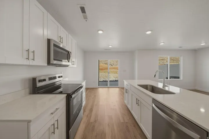 Bright kitchen featuring white cabinetry, stainless steel appliances, light-toned countertops, wood-finish flooring, and recessed lighting