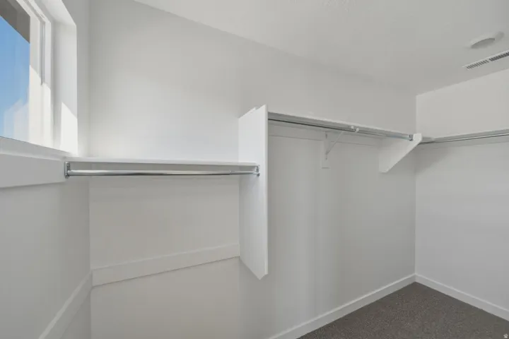 Walk-in closet featuring white walls, wall-mounted shelving, multiple clothing rods, and gray carpeting