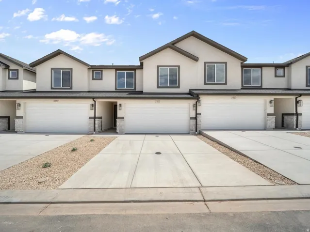 Contemporary stucco facade with dark trim windows, attached garages, stone accents, and concrete driveways