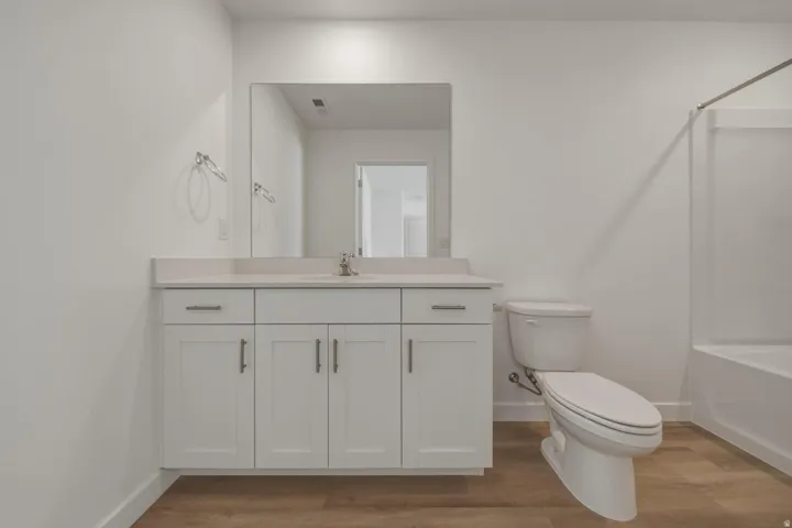 White vanity with a light-toned countertop, wood-finish flooring, and a white bathtub with a shower rod