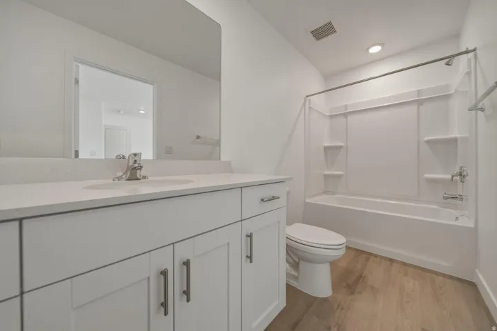 Bathroom featuring a white vanity with a light-toned countertop, an undermount sink, and wood-finish flooring