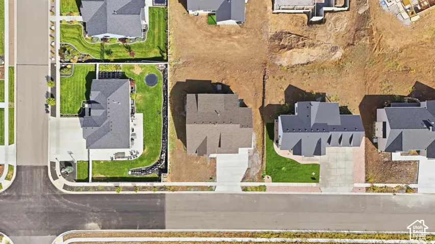 Aerial perspective showcasing a developed residential street, a property with a manicured lawn, an adjacent property with a paved driveway, and multiple houses with dark-toned roofs