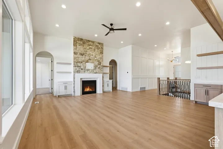 Spacious interior with vaulted ceilings, wood-finish flooring, a stone-clad fireplace, built-in cabinetry, and a ceiling fan