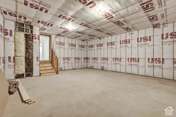 Unfinished interior space featuring wall and ceiling insulation, exposed wooden stairs, and a concrete floor