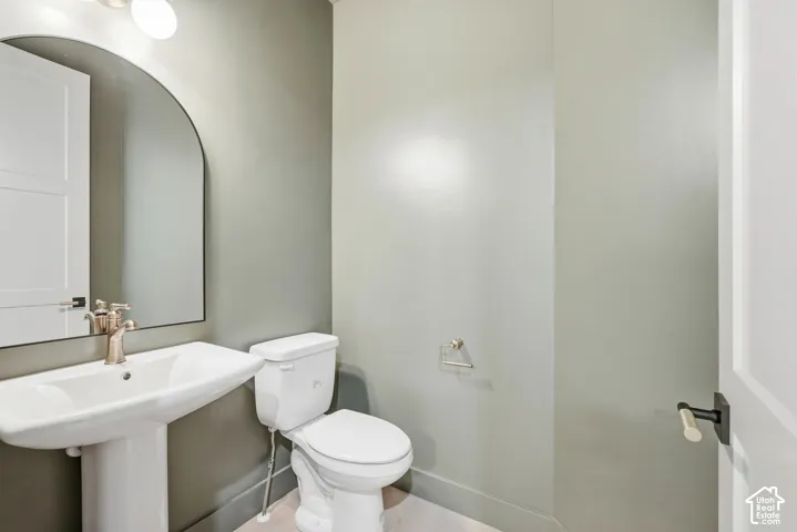 Pedestal sink with a brushed nickel faucet, arched mirror, recessed lighting, and a white two-panel door with black hardware