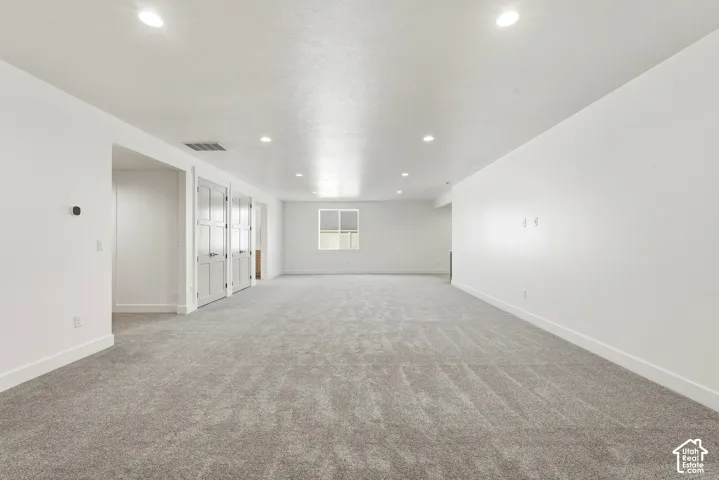 Spacious room featuring light gray carpeting, recessed lighting, and a window with white trim